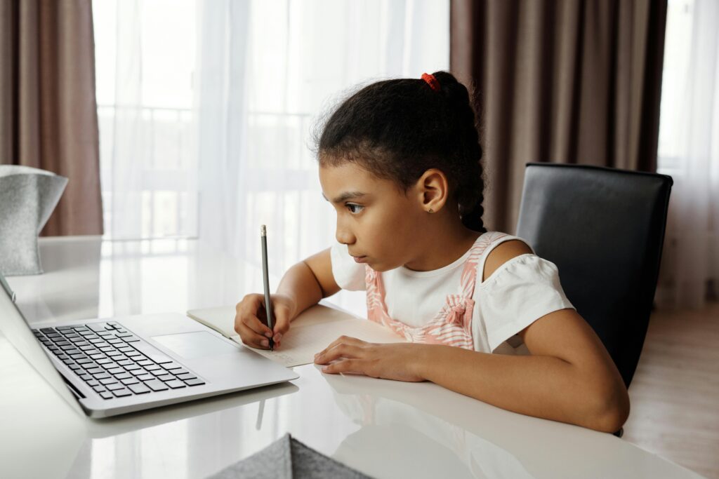 A girl writing and looking at a laptop